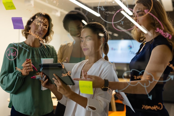 Foto diverse colleghe creative in discussione, brainstorming, prendendo appunti sulla parete di vetro dell'ufficio. ufficio casuale, brainstorming, affari, lavoro di squadra, affari, comunicazione e lavoro, inalterati.