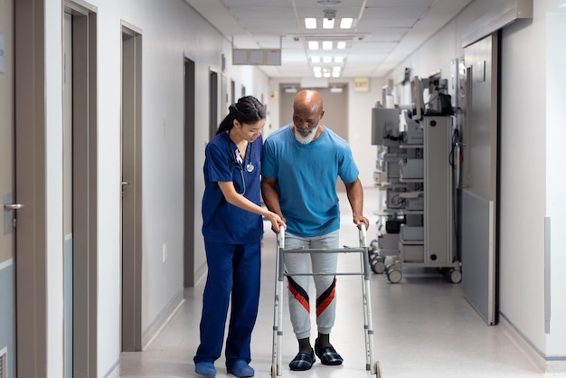 Diverse dottoresse che aiutano i pazienti maschi anziani a usare un telaio per camminare nel corridoio dell'ospedale, spazio di copia. Servizi ospedalieri, medici e sanitari.