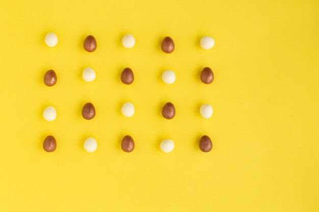 Diverse file di piccole uova fatte di cioccolato bianco e fondente su sfondo gialloCartolina d'auguri di Pasqua simbolo della celebrazione domenica di CristoHoliday composizione copia spazio per congratulazioni di testo