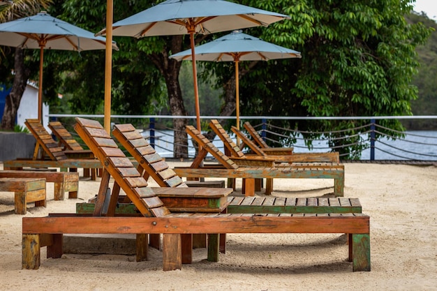 Diverse sedie a sdraio in legno vuote sulla sabbia sotto gli ombrelloni verdi
