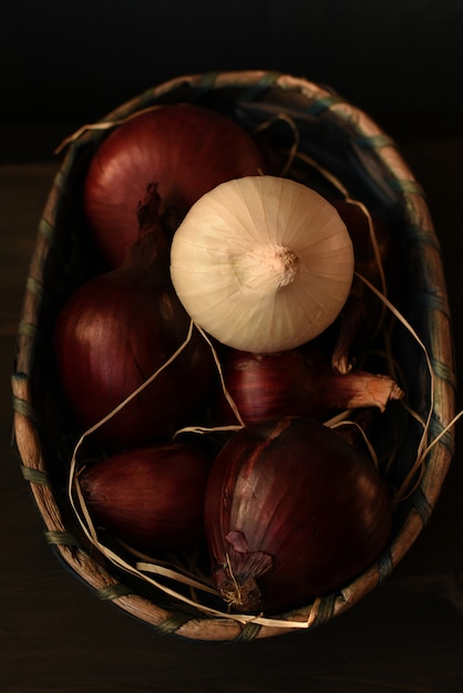 Diverse teste di cipolla rossa spagnola e una lampadina bianca sono piegate in un cesto di vimini. Sfondo marrone scuro
