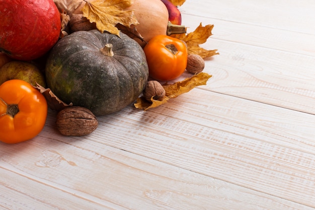 Diverse verdure, zucche, mele, pere, noci, pomodori e foglie secche su un fondo di legno bianco. Mood autunnale, copyspace. Vendemmia