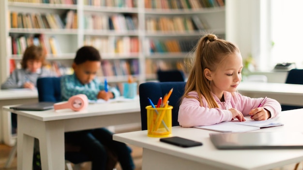 Diversi bambini seduti ai tavoli in classe alla scuola elementare o all'asilo scrivono o disegnano quaderni