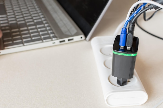 Diversi cavi collegati a un caricatore USB multiporta per scorrere lungo un laptop su una scrivania