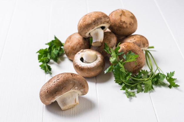 Diversi funghi reali con foglie di prezzemolo su un tavolo di legno bianco. Cibo vegetariano. Funghi coltivati artificialmente.