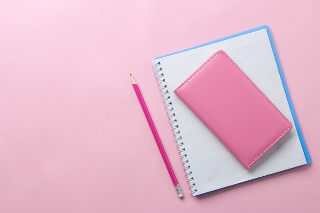 Diversi quaderni e una matita rosa su uno sfondo rosa brillante. vista dall'alto. strumenti per ufficio