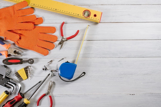 Diversi strumenti di costruzione o lavorazione e guanti flatlay su sfondo di legno bianco