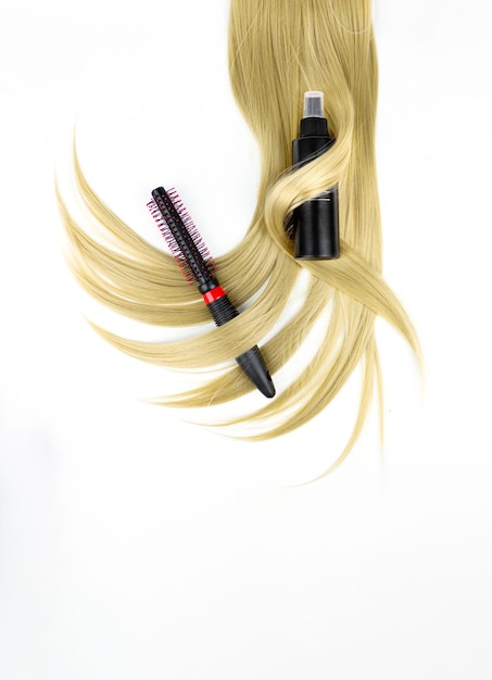 Diversi strumenti professionali per parrucchieri spazzola per capelli rotonda con lacca per capelli e ciocca di capelli biondi su sfondo bianco piatto Concetto di spa per la cura dei capelli