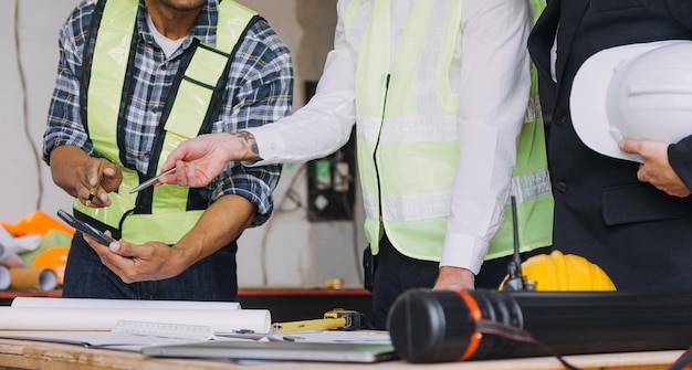 Diversi team di specialisti utilizzano il computer tablet sul progetto di costruzione di immobili in cantiere con ingegnere civile, architetto, investitore aziendale e lavoratore generale, discutendo i dettagli del piano