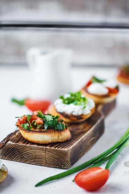 Diversi tipi di bruschette italiane con pomodori, mozzarella ed erbe su una tavola di legno