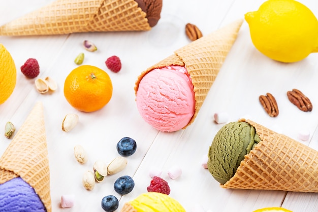 Diversi tipi di gelato in un cono di cialda con bacche e frutti su un tavolo di legno