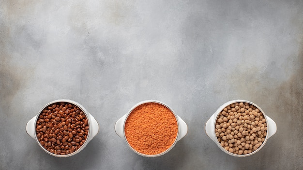 Diversi tipi di legumi: fagioli rossi, lenticchie rosse, banner di cibo vegetariano di ceci, posto per testo superficie in cemento grigio, vista dall'alto