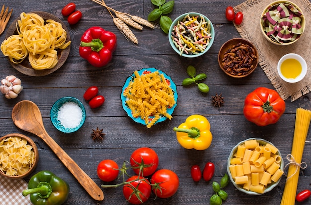 Diversi tipi di pasta con vari tipi di verdure su un tavolo di legno