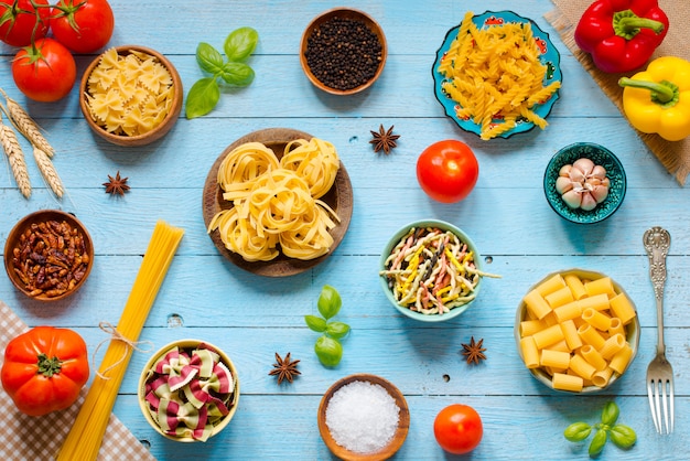 Diversi tipi di pasta con vari tipi di verdure su un tavolo di legno