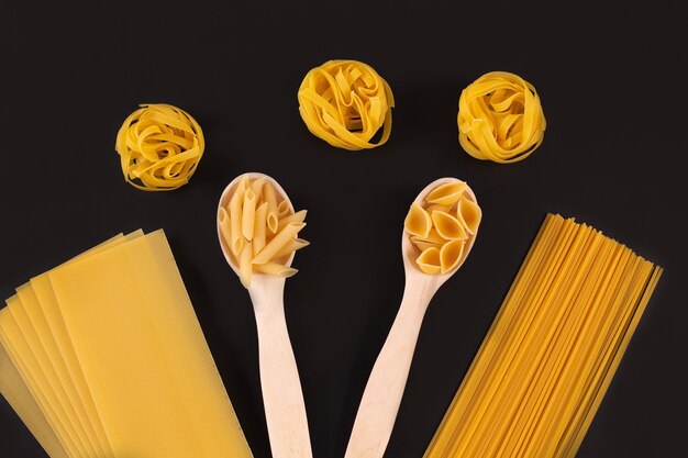 Diversi tipi di pasta in cucchiai di legno sul tavolo nero