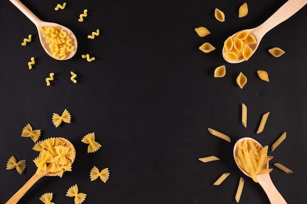 Diversi tipi di pasta in cucchiai di legno sul tavolo