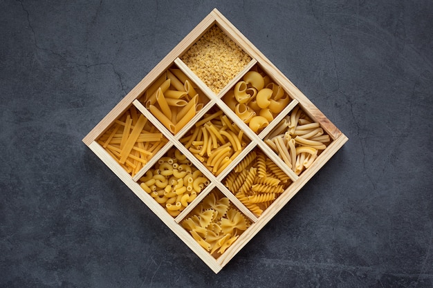 Diversi tipi di pasta in una scatola di legno su una superficie scura
