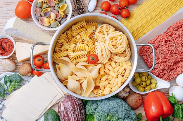 Diversi tipi di pasta italiana su fondo di legno con vari ingredienti per cucinare piatti della tradizione italiana