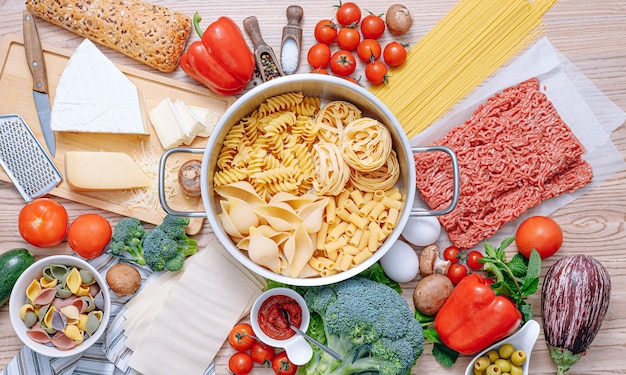 Diversi tipi di pasta italiana su fondo di legno con vari ingredienti per cucinare piatti della tradizione italiana