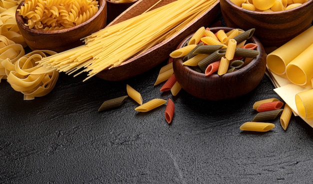 Diversi tipi di pasta su sfondo nero con copia spazio per il testo