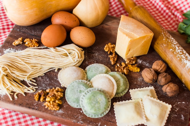 Diversi tipi di ravioli crudi con ingredienti sul tagliere di legno