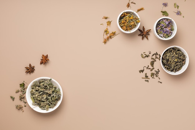 Diversi tipi di tè ed erbe aromatiche in ciotole su fondo beige
