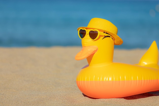 Divertente anatra gialla che indossa un cappello da spiaggia e occhiali da sole sullo sfondo blu del mare e del cielo Vacanze estive e concetto di viaggio