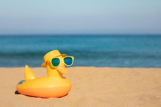 Divertente anatra gialla che indossa un cappello da spiaggia e occhiali da sole sullo sfondo blu del mare e del cielo Vacanze estive e concetto di viaggio