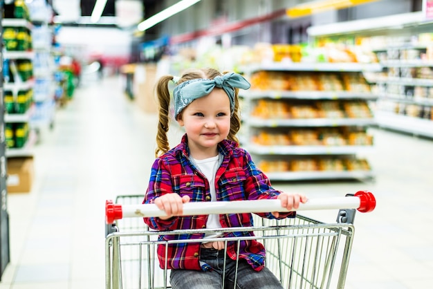 Divertente bambina bambino, seduto nel carrello durante la spesa in famiglia nell'ipermercato