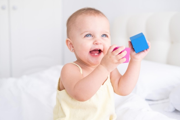 divertente bambina in tuta gialla che gioca con i cubi di legno dei bambini sul letto