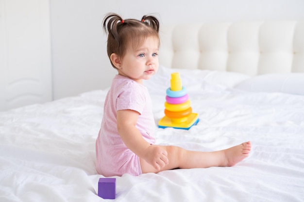 divertente bambina in tuta rosa che gioca con il giocattolo di plastica piramide per bambini sul letto