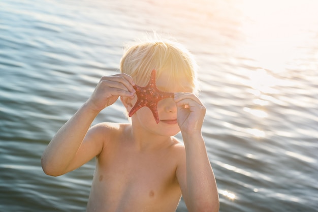 Divertente bambino biondo che gioca con le stelle marine. Vacanze al mare con bambini