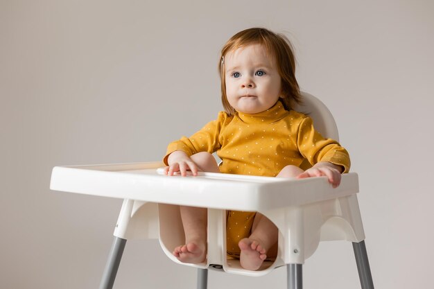 divertente bambino dagli occhi azzurri dai capelli rossi in un body giallo seduto su un seggiolone bianco