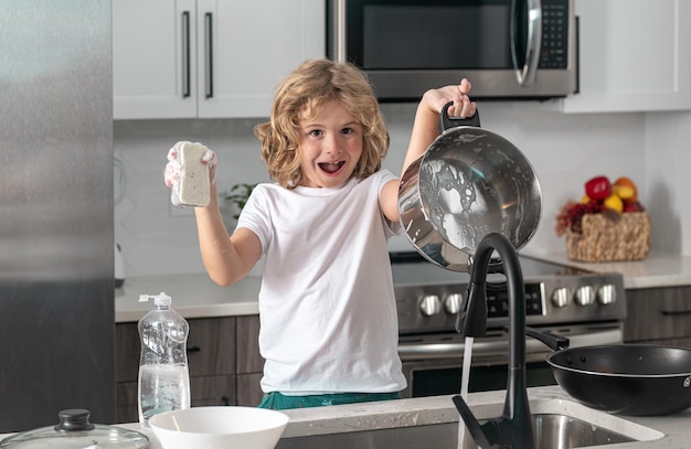 Divertente bambino eccitato che lava i piatti vicino al lavandino in cucina
