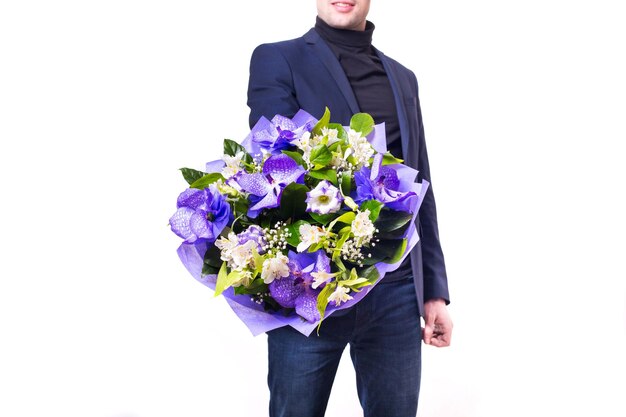 Divertente bel giovane con abito scuro con un bel bouquet nelle mani di fiori bianchi e viola isolati su sfondo bianco