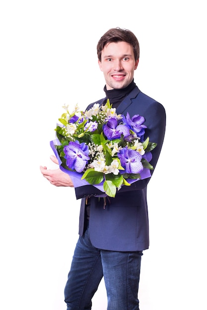 Divertente bel giovane con abito scuro con un bel bouquet nelle mani di fiori bianchi e viola isolati su sfondo bianco