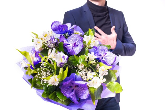 Divertente bel giovane con abito scuro con un bel bouquet nelle mani di fiori bianchi e viola isolati su sfondo bianco