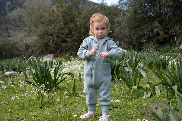 Divertente carino adorabile caucasica bionda bambina bambino in campo verde raccolta di fioriguardando la fotocameraBambino curiosokid infantlearning environmentnaturemountains in primavera o estate