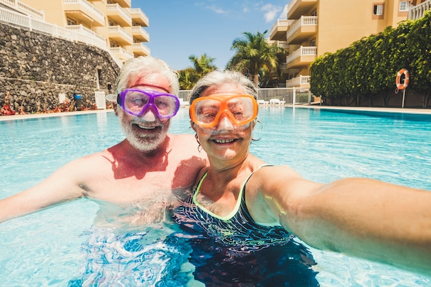 Divertente coppia di persone mature scattano foto selfie mentre si divertono e si divertono in piscina in residenza - anziano stile di vita felice in pensione con coppia anziana in attività di svago estivo insieme