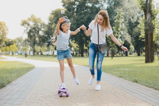 Divertente e gratuito. Sorridente ragazza in età prescolare attraente che si sente divertente e libera mentre usa il suo skateboard