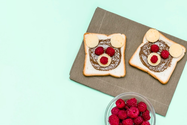 Divertente faccia di orso sandwich pane tostato con burro di arachidi formaggio e lampone su tovagliolo sfondo blu bambini bambino dolce dessert colazione pranzo cibo primo piano