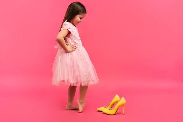 Divertente fashionista bambina in abito che indosserà le scarpe gialle della grande madre su sfondo colorato.