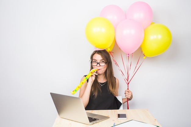 Divertente giovane donna che celebra il successo della sua attività o un compleanno in ufficio con palloncini colorati da festa.