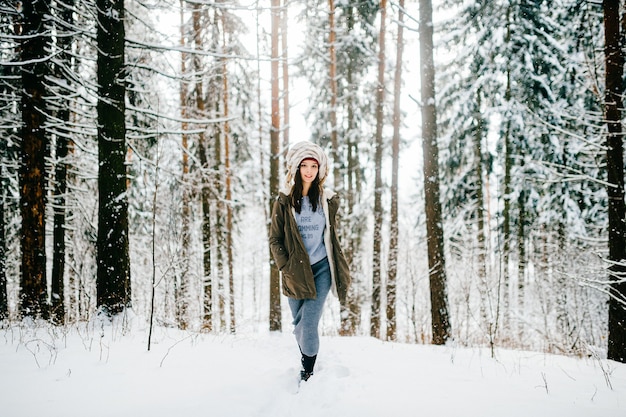 Divertente giovane ragazza attraente con un turbante dalla sciarpa che cammina nella foresta di neve