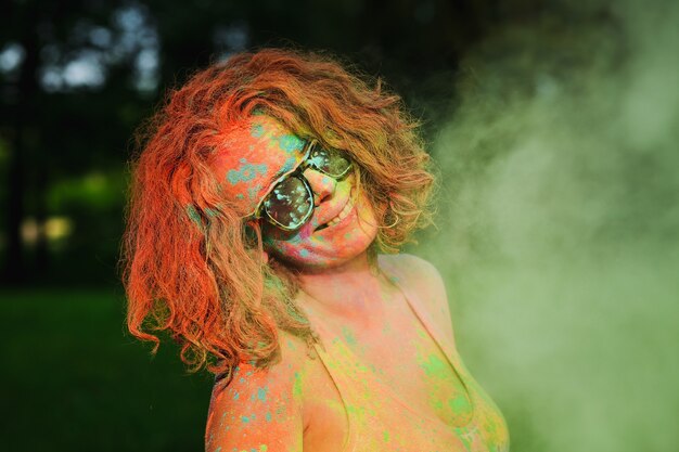 Divertente modella caucasica con gli occhiali, in posa in una nuvola di vernice Holi verde