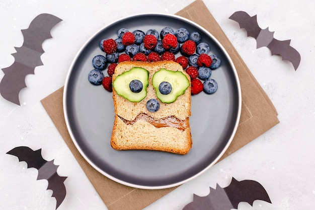 Divertente mostro spaventoso faccia sorriso su halloween sandwich pane tostato con burro di arachidi mirtillo lampone su platebats su sfondo grigio primo piano bambini bambino dolce dessert colazione pranzo cibo