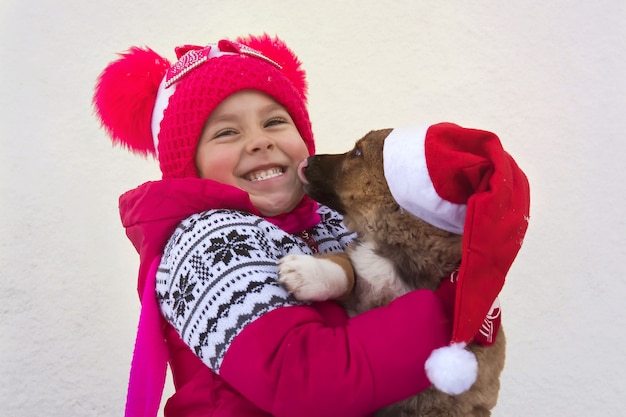 divertente piccolo bambino in babbo natale e cane bassotto. cucciolo di pastore tedesco che lecca la lingua faccia ridente del bambino. Berretto di babbo natale sul cane. Un simbolo del Natale e del nuovo 2018