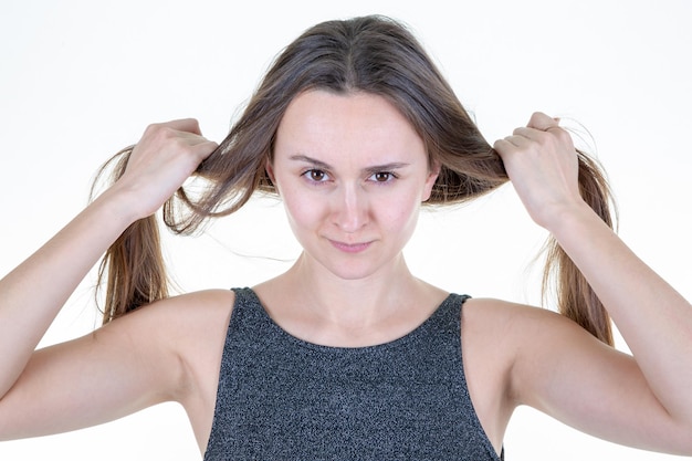 Divertente ragazza adulta divertendosi e facendo due code di cavallo con i suoi capelli castani su sfondo bianco