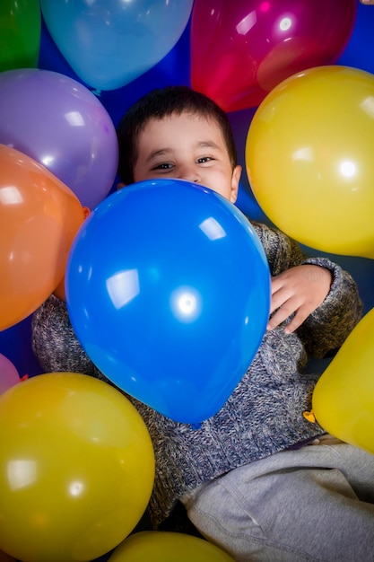 Divertente, ragazzo bruna che gioca con un sacco di palloncini colorati, sorrisi e gioia alla festa di compleanno