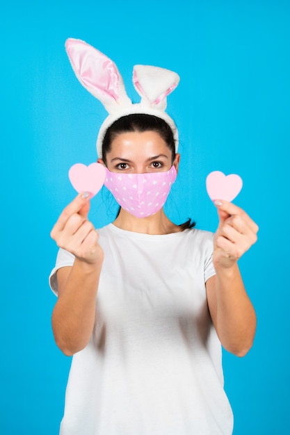 Divertente ritratto di donna che indossa orecchie da coniglio e maschera protettiva stampa cuore sul blu